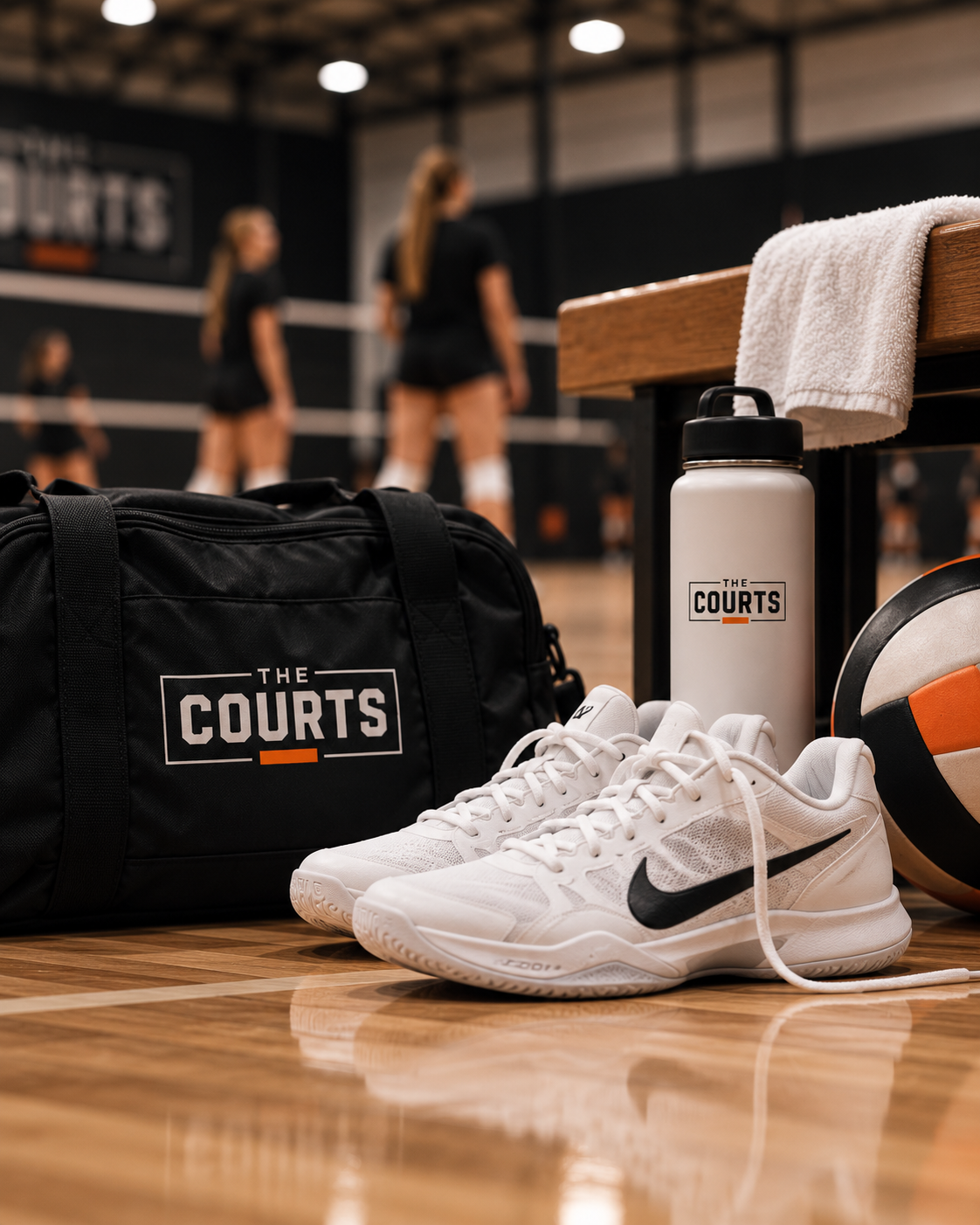 A Courts-branded duffel bag, water bottle, shoes, and volleyball courtside.