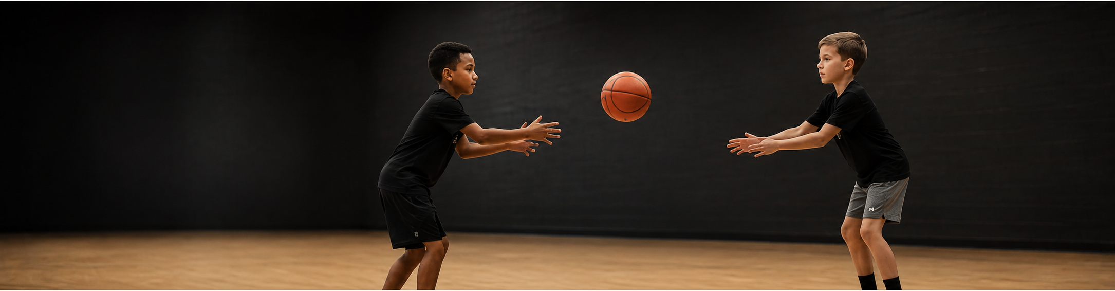 Two young athletes passing a basketball to each other on the court.