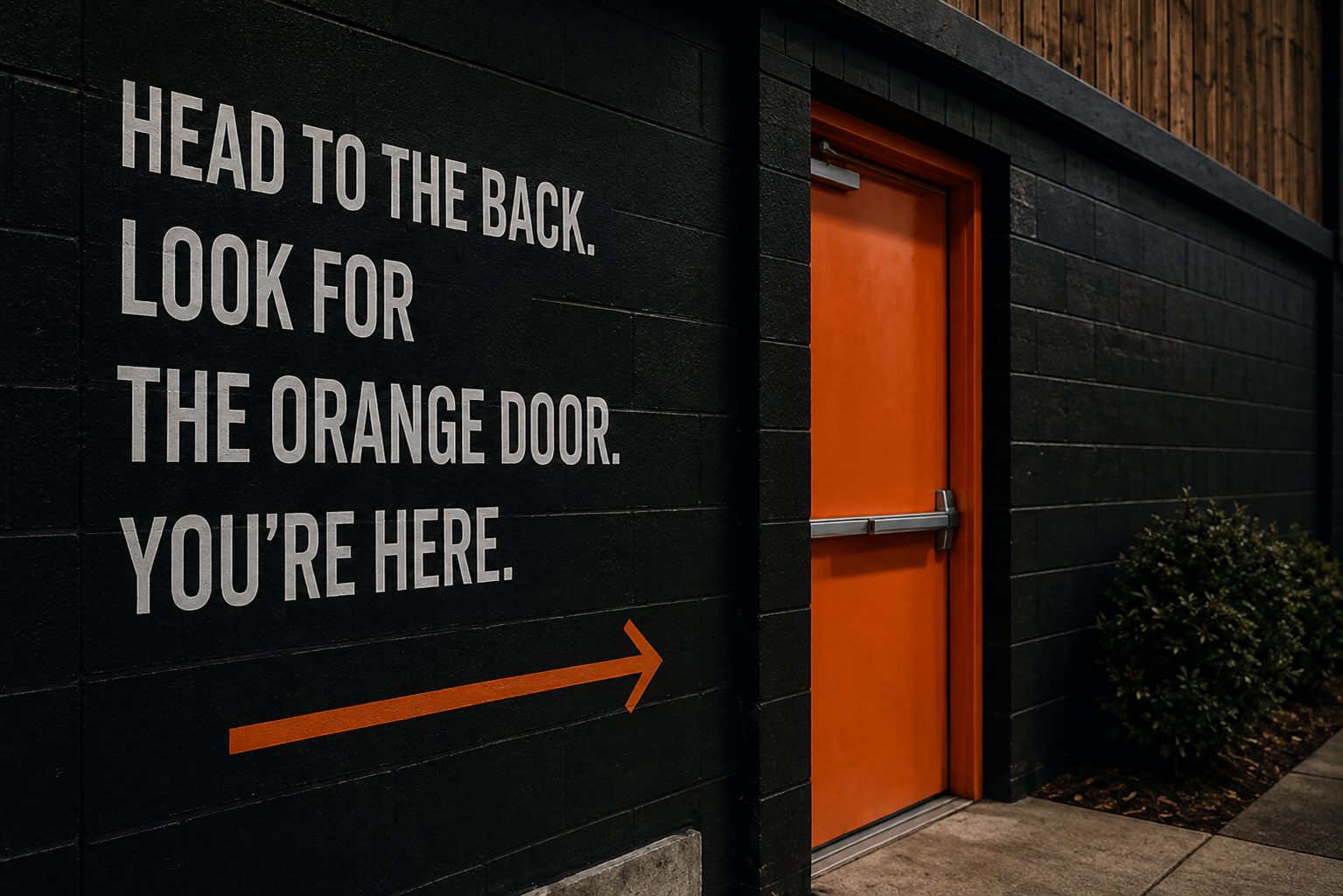 The black exterior wall of The Courts, with a bright orange door.