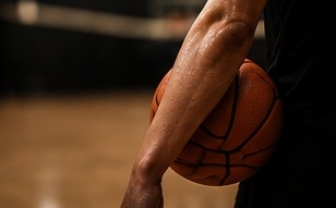 Close crop of an athlete's forearm resting against a basketball, mid-workout.